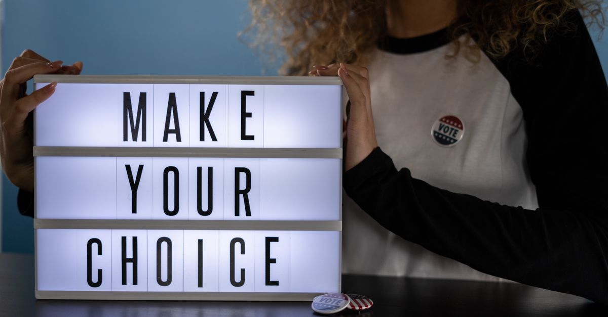Woman holding lightbox with 'Make Your Choice' promoting civic duty and voting.